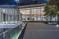 the glass facade has been lit up and reflected in the water of the pool at night