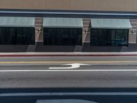 an empty street with arrows on the ground and building windows behind it, and two cars on the side of the road