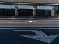 an empty street with arrows on the ground and building windows behind it, and two cars on the side of the road