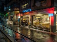 a restaurant called vacatera with a neon sign on the front window is a rain covered street in tokyo