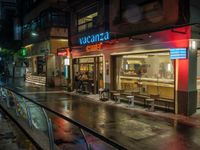 a restaurant called vacatera with a neon sign on the front window is a rain covered street in tokyo