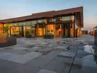 an outdoor area of some sort with lots of windows, flowers and a bench on the concrete floor