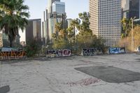 many buildings are in the background near graffiti covered parking lot's and there is graffiti on the ground