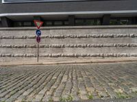 a cobblestone street next to two buildings with street signs on them, on a partly cloudy day