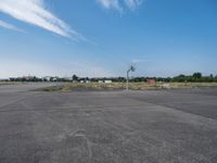 an empty parking lot is pictured from inside the picture while in focus there are trees and a red building in the background