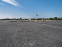 an empty parking lot is pictured from inside the picture while in focus there are trees and a red building in the background