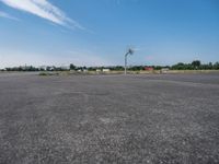 an empty parking lot is pictured from inside the picture while in focus there are trees and a red building in the background