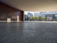 an empty street in the middle of some tall buildings, with concrete pillars, and one door open