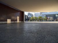 an empty street in the middle of some tall buildings, with concrete pillars, and one door open