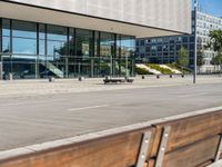 the sidewalk beside the building has a small brick bench next to it with a glass facade