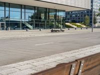 the sidewalk beside the building has a small brick bench next to it with a glass facade