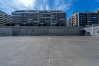 the empty parking lot in front of a wall with apartment buildings on it and a skateboarder on a ramp