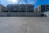 the empty parking lot in front of a wall with apartment buildings on it and a skateboarder on a ramp