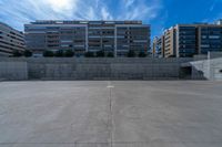 the empty parking lot in front of a wall with apartment buildings on it and a skateboarder on a ramp