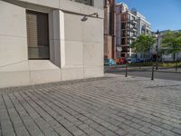 two people walking down an empty city street in an alley area with tall buildings in the background