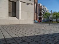 two people walking down an empty city street in an alley area with tall buildings in the background