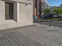 two people walking down an empty city street in an alley area with tall buildings in the background