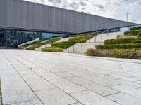 there is an outdoor area in front of a building with stairs and hedges that line it