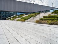 there is an outdoor area in front of a building with stairs and hedges that line it