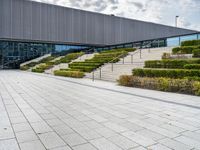 there is an outdoor area in front of a building with stairs and hedges that line it