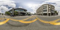 a street with yellow stripes on the ground and buildings around it is shown as a fisheye lens