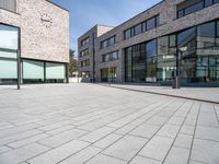 an open brick plaza in a city with modern architecture, and many windows, on a sunny day