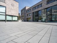 an open brick plaza in a city with modern architecture, and many windows, on a sunny day