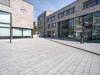 an open brick plaza in a city with modern architecture, and many windows, on a sunny day