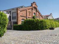 a large bricked walkway that is surrounded by bushbery and bushes, next to a brick building with red brick accents