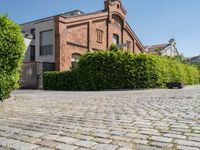 a large bricked walkway that is surrounded by bushbery and bushes, next to a brick building with red brick accents