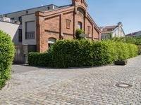 a large bricked walkway that is surrounded by bushbery and bushes, next to a brick building with red brick accents