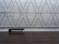 a wooden bench in front of a concrete wall and wood flooring with a small wooden plank underneath