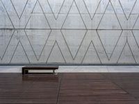 a wooden bench in front of a concrete wall and wood flooring with a small wooden plank underneath