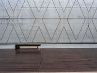 a wooden bench in front of a concrete wall and wood flooring with a small wooden plank underneath