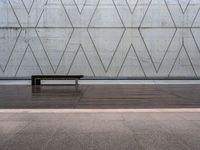 a wooden bench in front of a concrete wall and wood flooring with a small wooden plank underneath