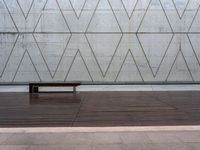 a wooden bench in front of a concrete wall and wood flooring with a small wooden plank underneath