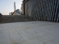 the view of a building from across the concrete walkway outside the building with no roof