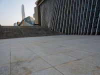 the view of a building from across the concrete walkway outside the building with no roof