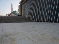 the view of a building from across the concrete walkway outside the building with no roof