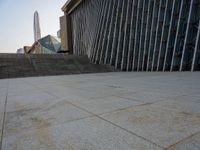 the view of a building from across the concrete walkway outside the building with no roof