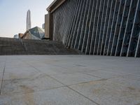 the view of a building from across the concrete walkway outside the building with no roof