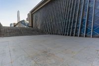 the view of a building from across the concrete walkway outside the building with no roof