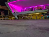 a purple lit building is on the street with a man walking across the sidewalk in front