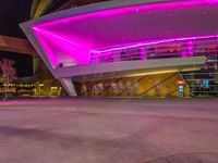 a purple lit building is on the street with a man walking across the sidewalk in front