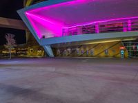 a purple lit building is on the street with a man walking across the sidewalk in front