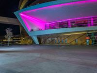 a purple lit building is on the street with a man walking across the sidewalk in front