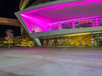 a purple lit building is on the street with a man walking across the sidewalk in front