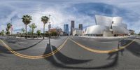 a 360 view of an intersection in front of buildings with curved road markings and trees