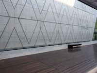 a bench is on the wooden floor in front of a large concrete wall at the park