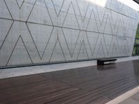 a bench is on the wooden floor in front of a large concrete wall at the park